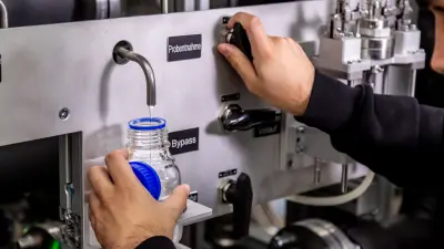 Technician taking sample of deionized water from equipment for PEM electrolysis stack quality analysis